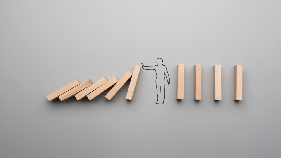 Wooden blocks fall, a cartoon silhouette stops the chain reaction with one hand.