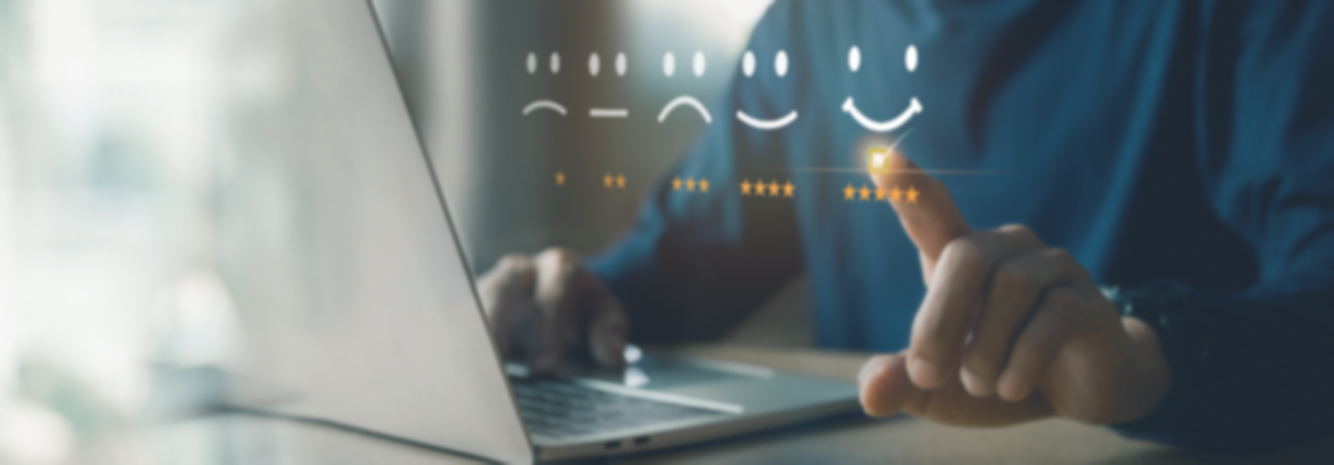 Person pekar på ett digitalt betygssystem med nöjda och missnöjda ansikten framför en laptop.