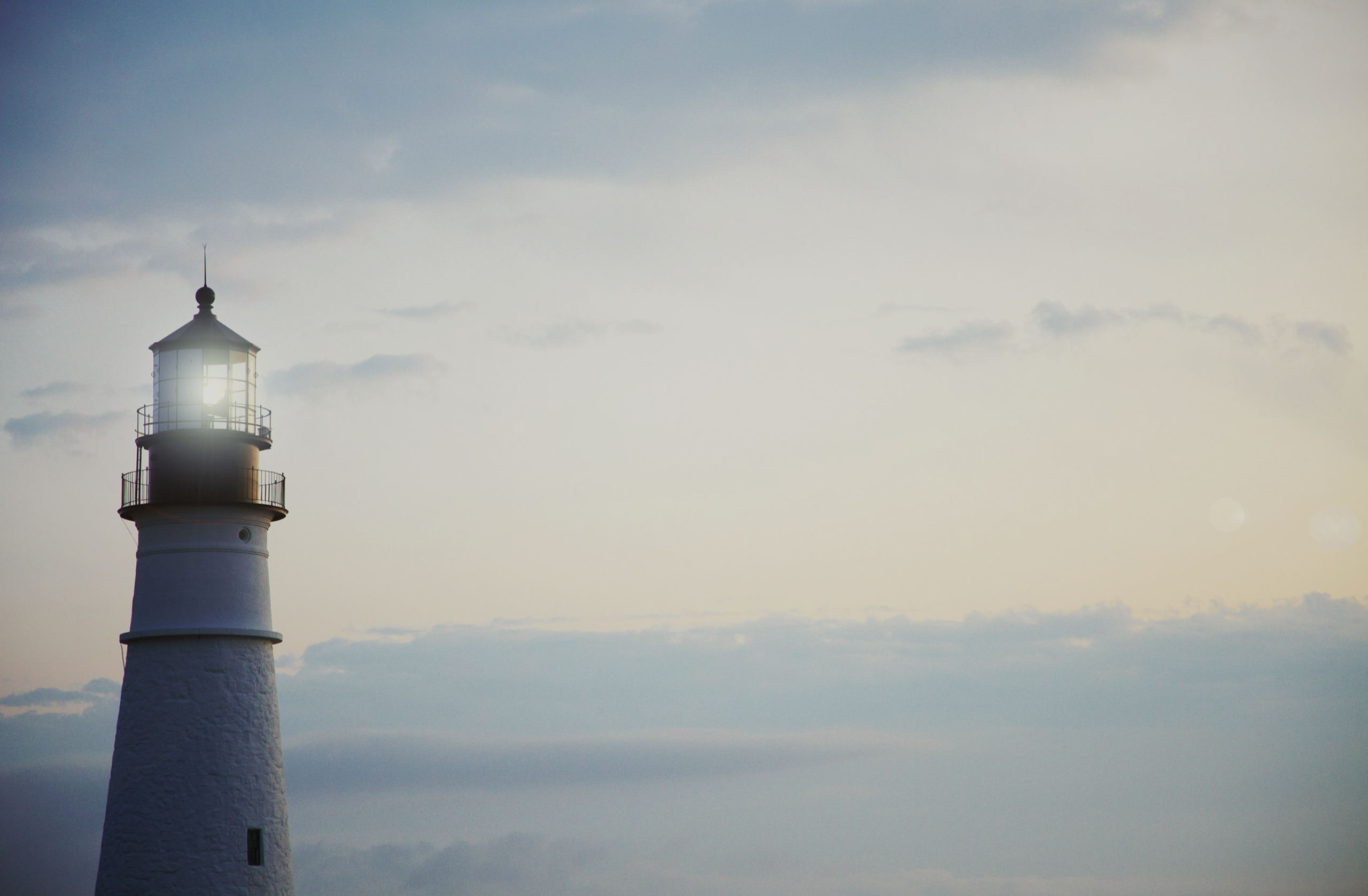 Lighthouse shines in the evening with cloudy sky in the background.