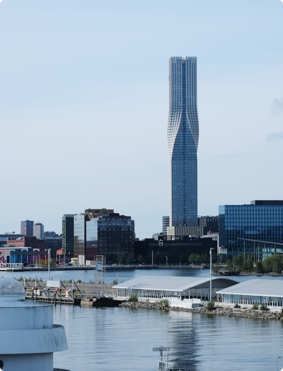 Hög byggnad med unik design vid vattnet, omgiven av lägre hus och modern stadsbebyggelse.