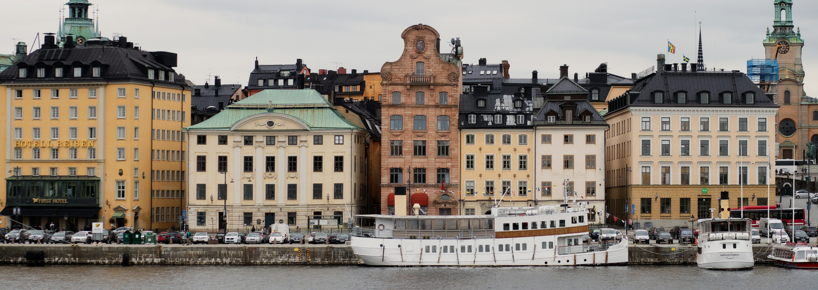 Facades of old buildings by the water in Gamla stan, Stockholm, with boats moored in front.
