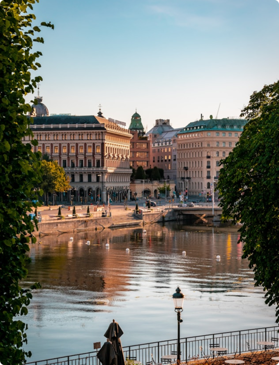 Gamla byggnader vid vattnet i centrala Stockholm, omgivna av träd och speglingar i vattnet.