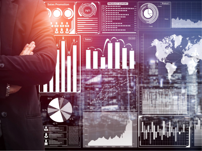 Person in a suit with crossed arms in front of several digital charts, bar graphs and a world map.