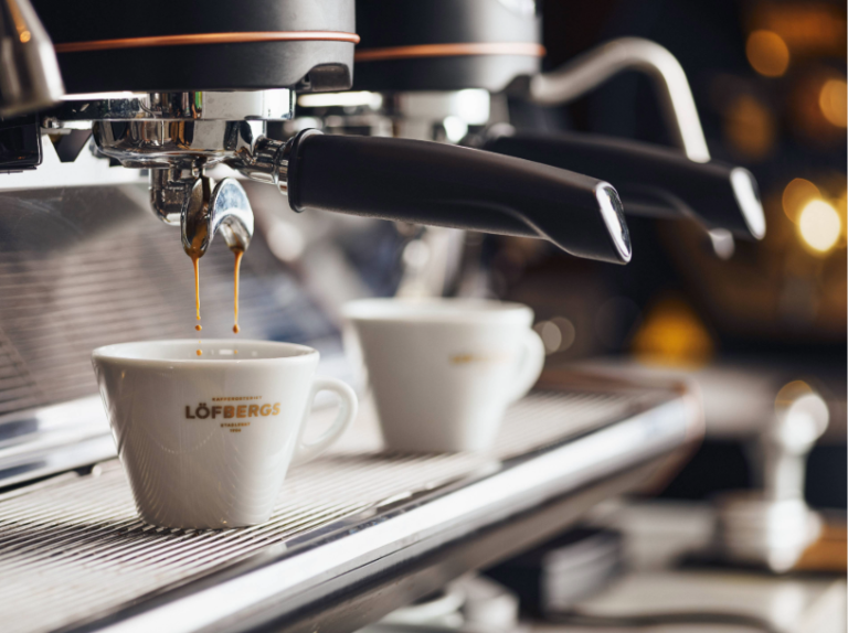 Närbild på espressomaskin som brygger kaffe i en kopp med Löfbergs-logo.