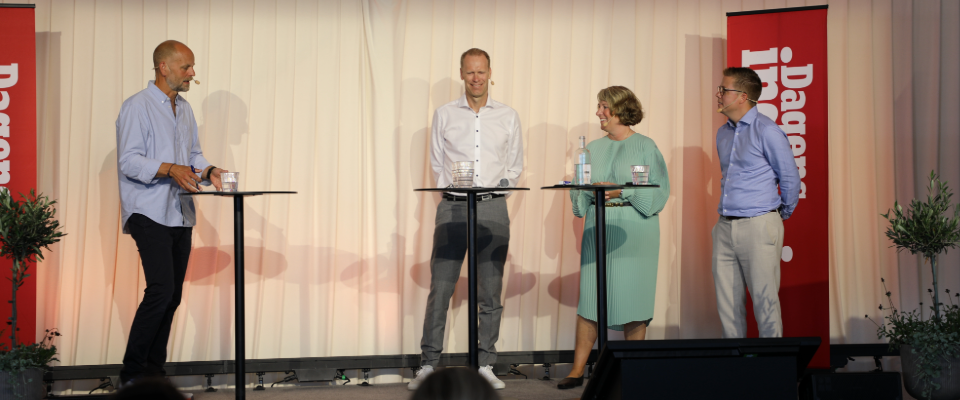 Fyra personer står på en scen och deltar i ett panelsamtal, två röda skyltar med texten "Dagens" syns bakom.